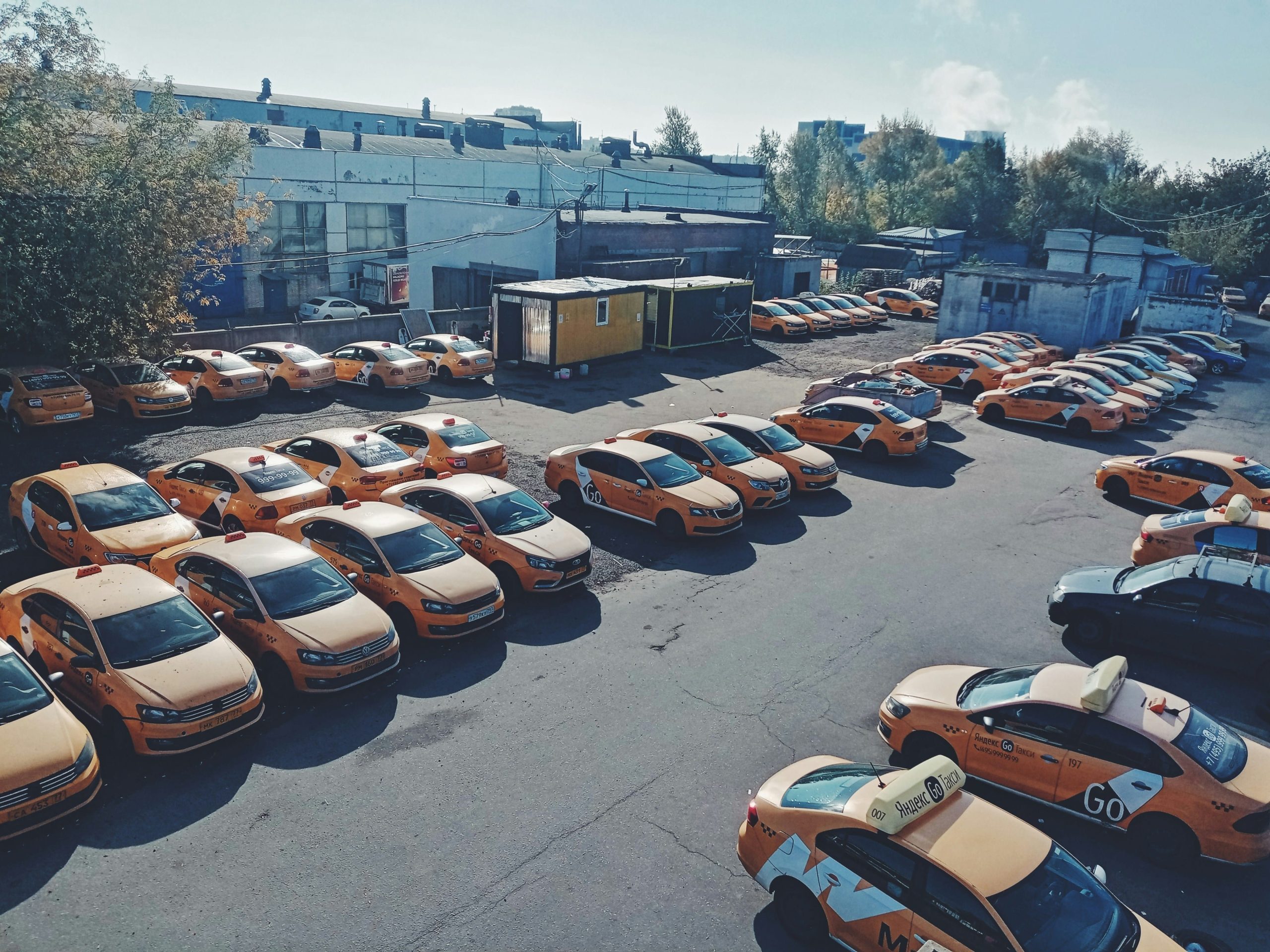 Zahlreiche orangefarbene Taxis sind in einem Hof geparkt, ideal für Fahrzeugortungslösungen.