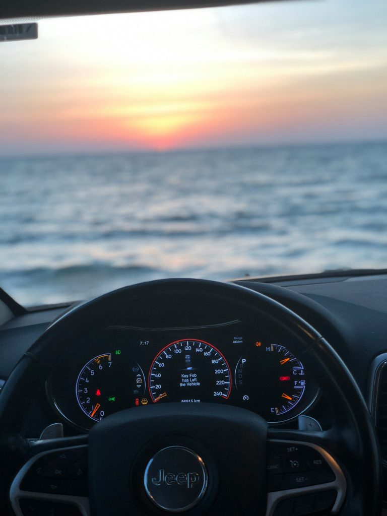 Ein Jeep-Armaturenbrett zeigt bei Sonnenuntergang über dem Meer, wie GPS Ortung bei der Fahrzeugortung helfen kann.
