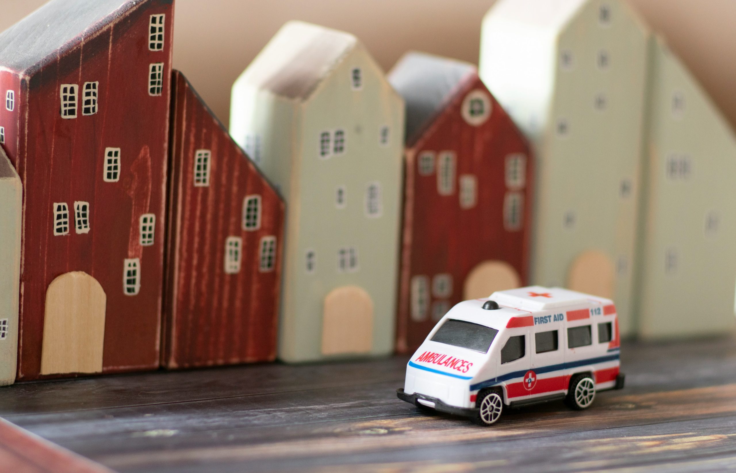Ein Spielzeugkrankenwagen fährt vor bunten Holzgebäuden, ideal für GPS Ortung in einer Miniaturstadt.