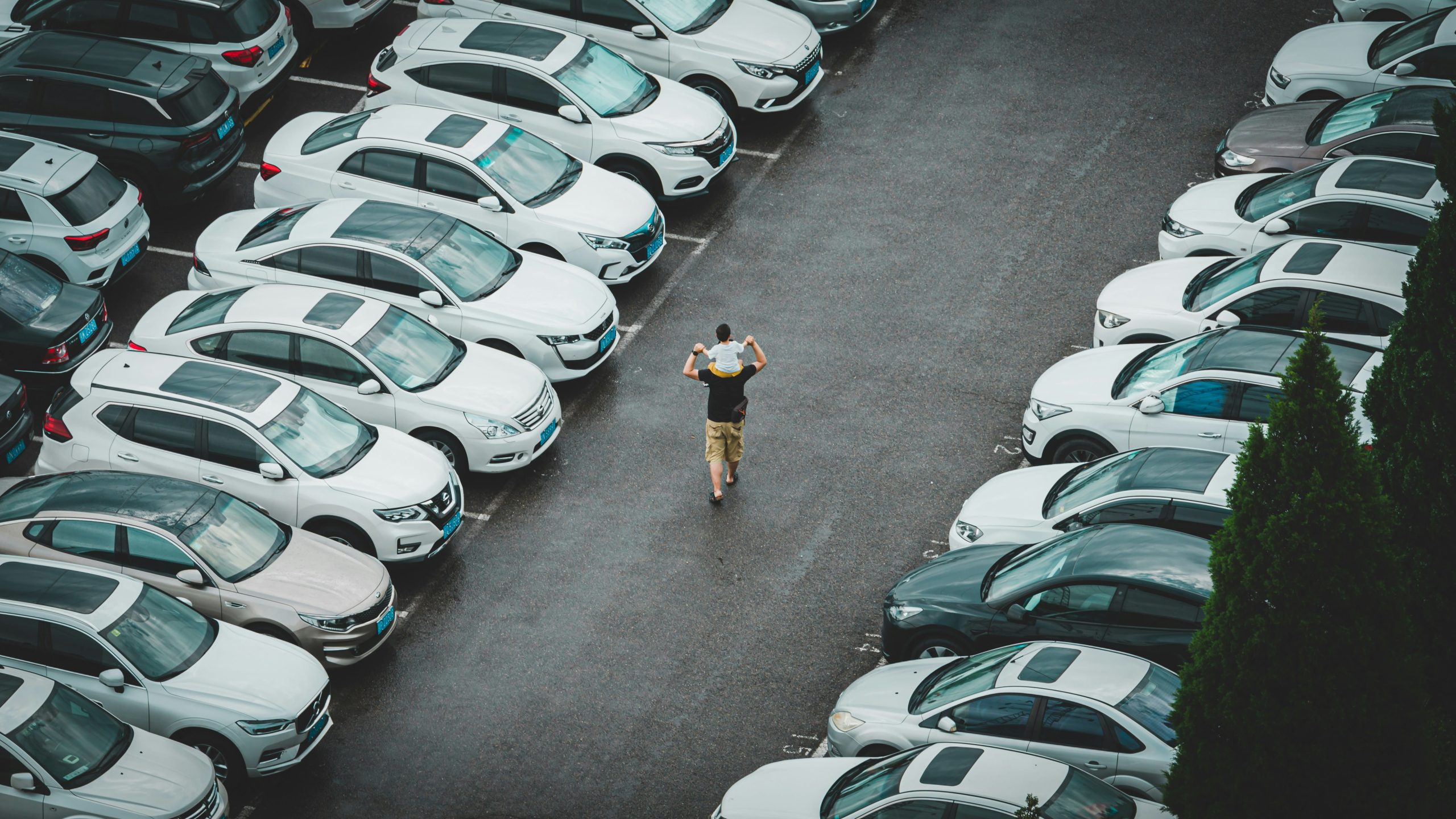 Ein Mann steht auf einem Parkplatz voller Autos, ideal für moderne Fahrzeugortungslösungen.